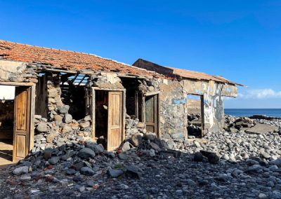 Baufälliges Haus am Steinstrand mit Meer dahinter